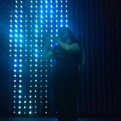 GIF of storyteller Kat Vancil doing her signature Happy Kitty Dance in front of a colorful rainbow light art installation. 